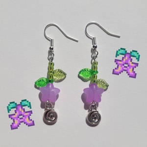 May include: A pair of purple flower earrings with green leaves and silver beads. The earrings have a silver swirl charm at the bottom.