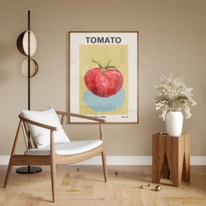 May include: A minimalist poster with a yellow background and a red tomato on a blue circle. The poster is framed in wood and has the word "TOMATO" in black text at the top. The poster is hanging on a beige wall above a wooden side table with a white vase and a bouquet of dried white flowers.