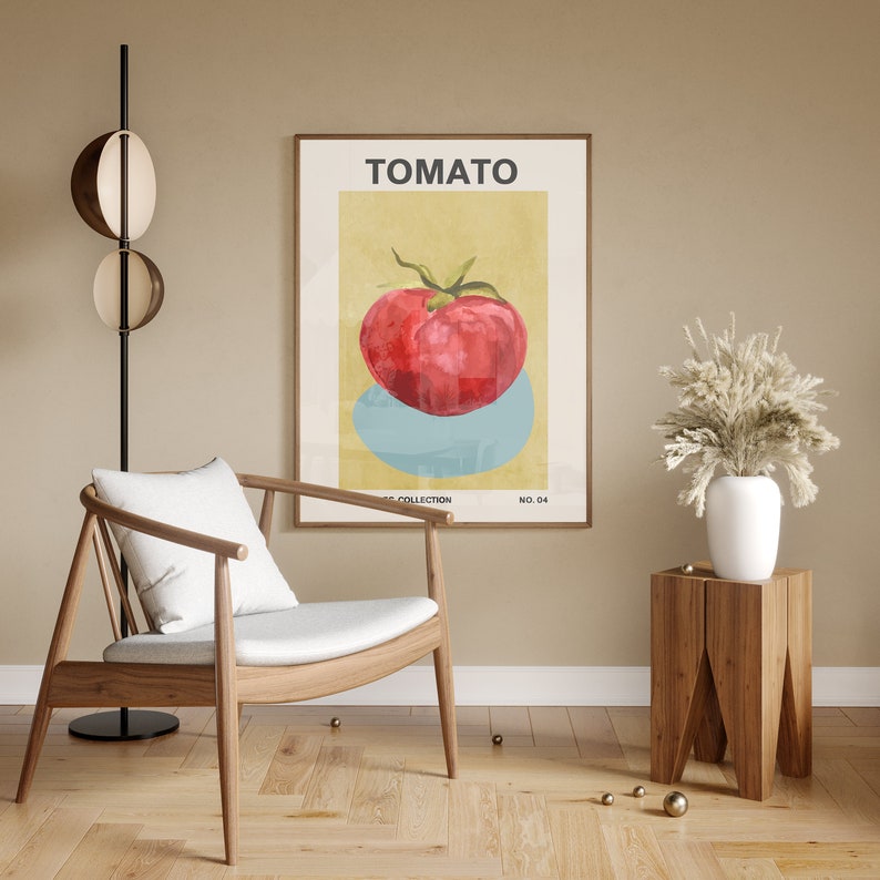May include: A minimalist poster with a yellow background and a red tomato on a blue circle. The poster is framed in wood and has the word "TOMATO" in black text at the top. The poster is hanging on a beige wall above a wooden side table with a white vase and a bouquet of dried white flowers.