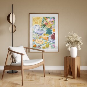Pode incluir: Uma pintura de uma natureza morta com frutas, flores e um bule de ch&aacute; em uma mesa. A pintura est&aacute; em uma moldura de madeira clara e est&aacute; pendurada em uma parede bege. Uma cadeira de madeira com um almofada branca est&aacute; em primeiro plano.