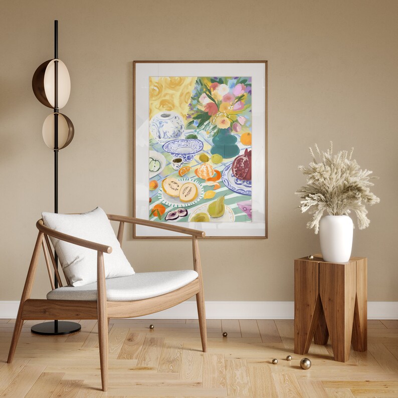 Pode incluir: Uma pintura de uma natureza morta com frutas, flores e um bule de ch&aacute; em uma mesa. A pintura est&aacute; em uma moldura de madeira clara e est&aacute; pendurada em uma parede bege. Uma cadeira de madeira com um almofada branca est&aacute; em primeiro plano.