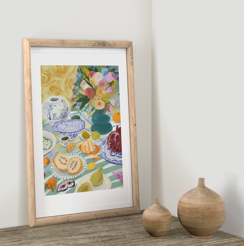 Pode incluir: Uma pintura emoldurada de uma natureza morta com um vaso de porcelana azul e branco cheio de flores coloridas, frutas e um prato com um padr&atilde;o azul e branco. A pintura est&aacute; colocada contra uma parede branca.