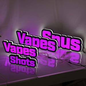 May include: Three illuminated signs with bright purple lettering and white outlines. The signs display the words Vapes, Snus, and Shots in a bold, blocky font. Each sign features a thin white power cord extending from the side, casting a glow.