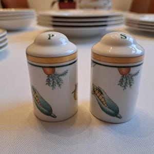 May include: Two white ceramic salt and pepper shakers with a yellow band and green and yellow corn on the side. The shakers are labeled "P" and "S" on the top.