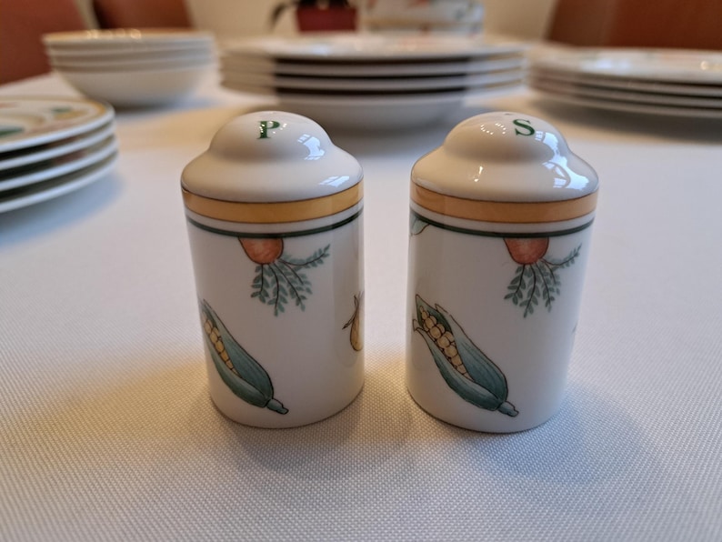 May include: Two white ceramic salt and pepper shakers with a yellow band and green and yellow corn on the side. The shakers are labeled "P" and "S" on the top.
