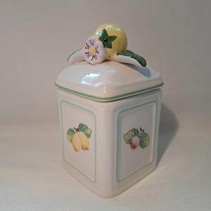 May include: White ceramic canister with a green and yellow lemon design. The lid has a 3D lemon and flower detail.