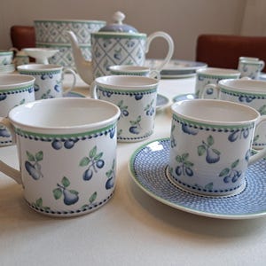 May include: A white porcelain tea set with a blue and green fruit pattern. The set includes mugs, saucers, a teapot, and serving bowls. The mugs have a handle and are decorated with blue plums and green leaves. The saucers have a blue dotted pattern.