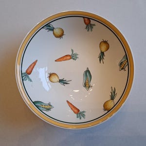 May include: A white ceramic bowl with a yellow rim features a pattern of carrots, onions, and corn on a white background.