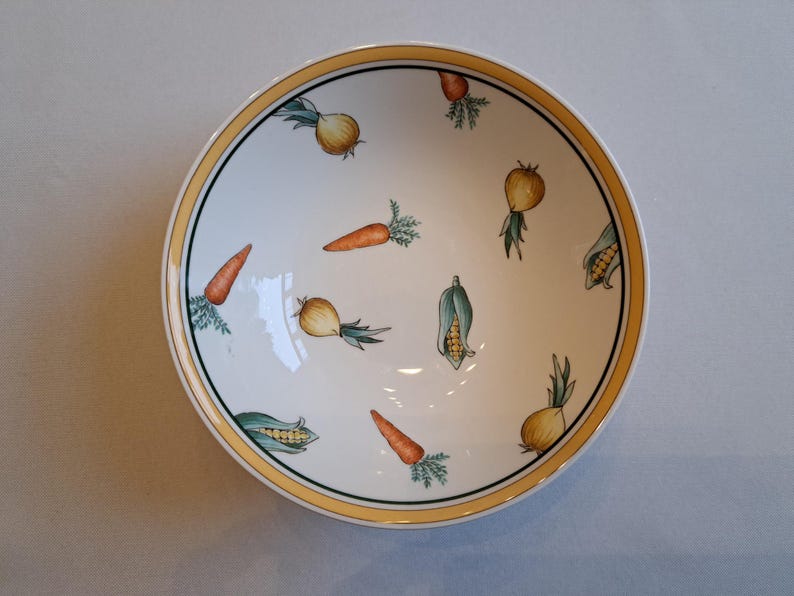 May include: A white ceramic bowl with a yellow rim features a pattern of carrots, onions, and corn on a white background.