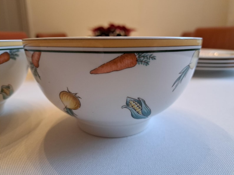 May include: Two white ceramic bowls with a yellow rim and a vegetable design. The bowls feature carrots, onions, and corn.