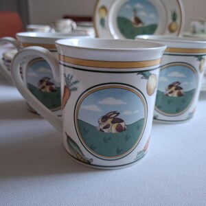 May include: Set of four white ceramic teacups with a green, yellow, and brown floral design featuring rabbits and carrots.