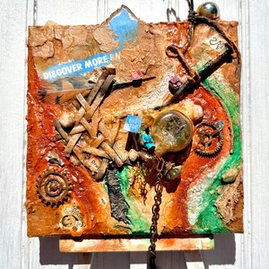 May include: Mixed media art piece with a textured, layered surface. Features a collage of materials including wood, metal gears, and a glass orb. Includes text that reads "DISCOVER MORE" and a miniature "BUS STOP" sign.
