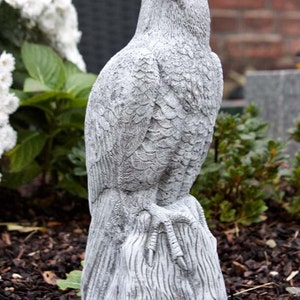 Könnte beinhalten: Eine detaillierte, graue Betonstatue eines Raubvogels, möglicherweise eines Falken, der auf einem Baumstumpf sitzt. Die Statue hat strukturierte Federn und scharfe Krallen, mit einem fokussierten Blick. Für Gartendekoration.
