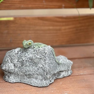 Op de afbeelding: Een klein groen hagedisbeeldje dat op een grijze rots zit, een decoratief tuinaan accent.