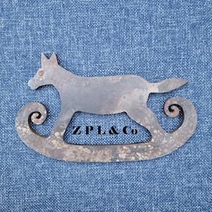 May include: A metal rocking horse silhouette with the text "ZPL & Co" on a blue denim background. The horse is a light brown color with a distressed finish, and the rockers have a curled design.
