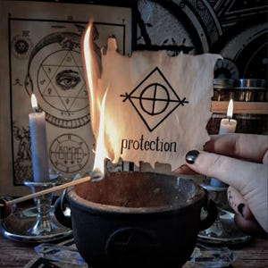 Puede incluir: Un pergamino en llamas con la palabra "protección" y un símbolo geométrico sobre un caldero negro. Dos velas encendidas y diagramas ocultos en el fondo crean una atmósfera mística.