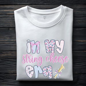 Könnte beinhalten: Weißes T-Shirt mit Rundhalsausschnitt und dem Text "in my string cheese era" in einer verspielten Schriftart. Die Buchstaben sind mit Mustern wie rosa Vichy, Blumen und blauen Streifen verziert. Eine dekorative Käse-Grafik ist ebenfalls enthalten.