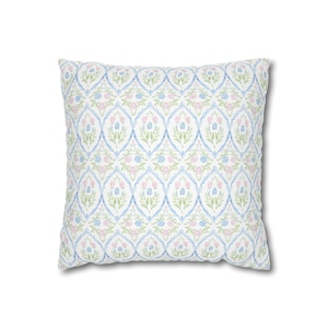 May include: Square cushion featuring a repeating pattern of blue, pink, and green floral designs on a white background. The pattern includes stylized flowers and leaves within a lattice structure. The cushion has a soft, textured appearance.