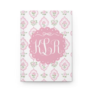 May include: A pink and white notebook with a floral pattern and a pink monogram with the letters "KLR" in white.