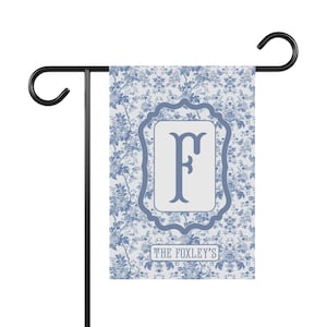 May include: A blue and white garden flag with a floral pattern and the letter "F" in a decorative frame. The text "The Foxley's" is at the bottom of the flag.