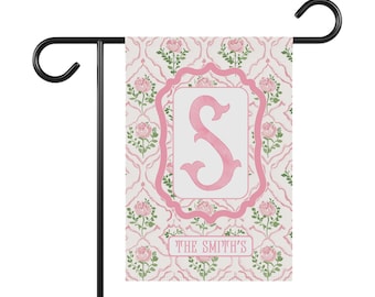 Könnte beinhalten: Eine rosa-weiße Gartenflagge mit einem rosa Buchstaben "S" in einem dekorativen Rahmen. Die Flagge hat ein Blumenmuster und den Text "THE SMITH'S" unten.