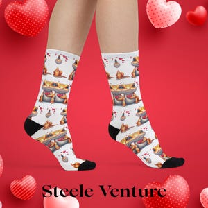 Puede incluir: Calcetines blancos con un patrón repetido de ranas de dibujos animados sosteniendo corazones, con acentos de corazón rojo. Los calcetines tienen talones y dedos negros. El fondo es rojo con decoraciones de corazón. El texto "Steele Venture" está en la parte inferior.