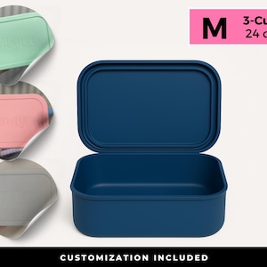 May include: A navy blue rectangular lunch box with an open lid. The box is labeled "M" and "3-Cup 24 oz" in a pink rectangle. Three smaller, pastel-colored lids are shown with custom text. The bottom of the image reads "CUSTOMIZATION INCLUDED".