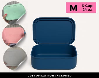 Puede incluir: Una fiambrera rectangular azul marino con tapa abierta. La caja está etiquetada con "M" y "3-Cup 24 oz" en un rectángulo rosa. Se muestran tres tapas más pequeñas de colores pastel con texto personalizado. La parte inferior de la imagen dice "CUSTOMIZATION INCLUDED".