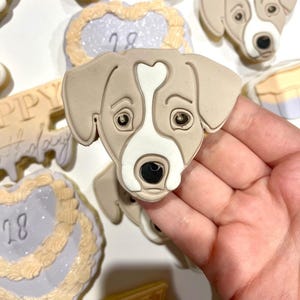 Puede incluir: Una colección de galletas de azúcar decoradas con la cara de un perro, una galleta en forma de corazón con el número 18 y una galleta con el texto "Feliz cumpleaños".