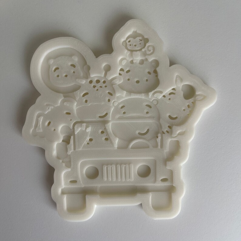 May include: White silicone mold of a jeep with a monkey, giraffe, hippopotamus, and zebra riding in it.