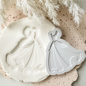 Peut inclure: Un moule en silicone blanc pour la pâtisserie ou l'artisanat, présentant un design détaillé d'une princesse en robe. Le moule est présenté à côté d'un design similaire, mais en blanc uni.