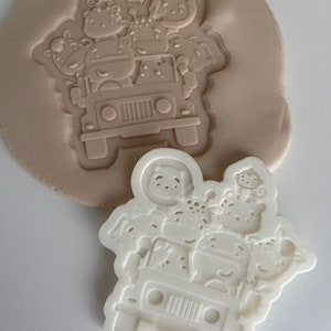 May include: White plastic cookie cutter shaped like a jeep with animals on top. The animals include a giraffe, a monkey, a hippopotamus, a zebra, and a lion.