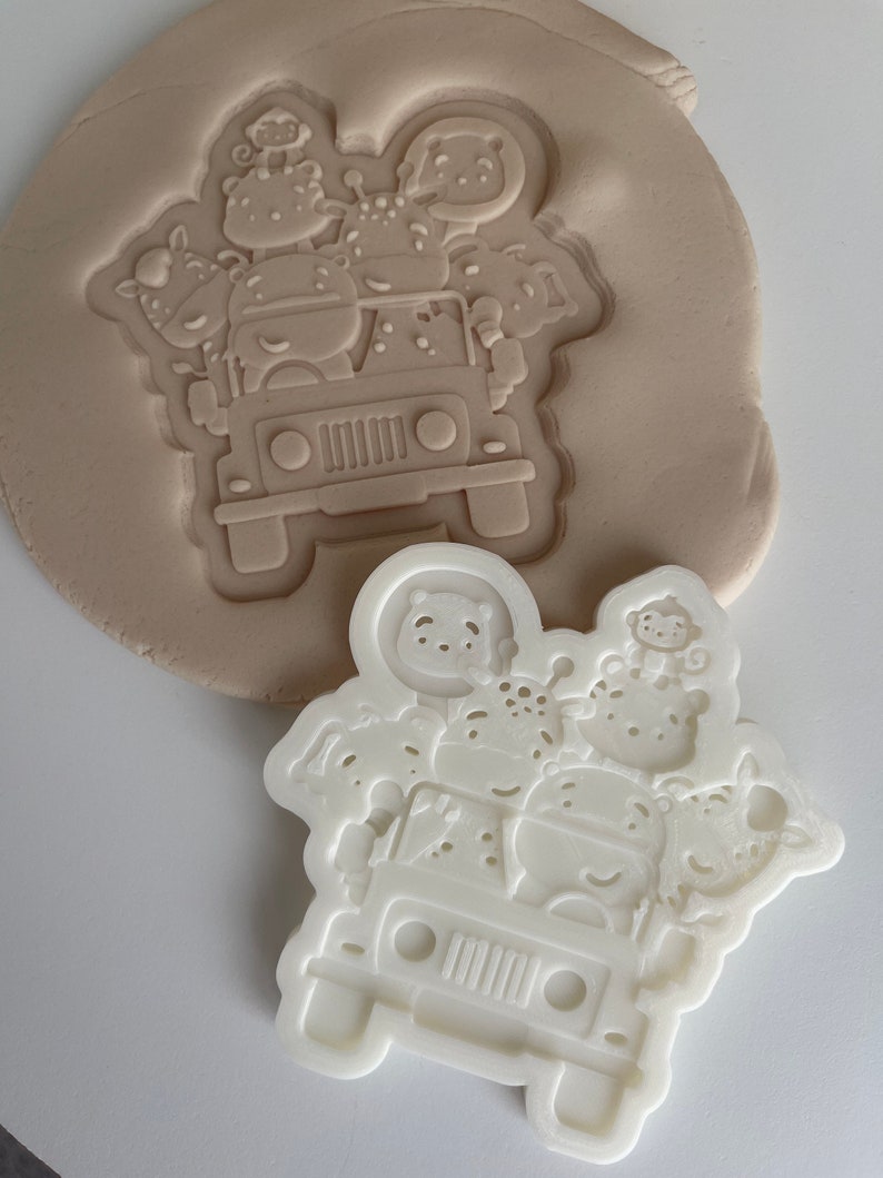 May include: White plastic cookie cutter shaped like a jeep with animals on top. The animals include a giraffe, a monkey, a hippopotamus, a zebra, and a lion.