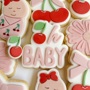 May include: A set of pink and white decorated sugar cookies with cherry and baby themes. The cookies feature cherries, bows, and the text "Oh Baby".