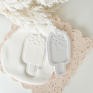 Puede incluir: Molde de helado de plástico blanco sobre un fondo blanco. El molde tiene forma de helado de paleta con chispas de chocolate en la parte superior.