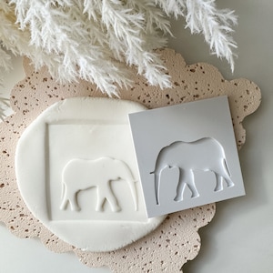 May include: White silicone mould with an elephant design. The mould is shown next to a white clay impression of the elephant.