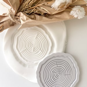Puede incluir: Dos moldes de silicona blancos con un diseño de anillo de árbol. Los moldes están sobre una superficie blanca.