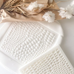 May include: Two white silicone molds for baking, one with a raised textured pattern of small circles and the other with a raised textured pattern of a grid.