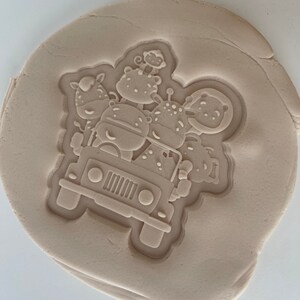 May include: A white clay mold with a raised design of a jeep with a monkey, zebra, giraffe, and hippopotamus riding in it.