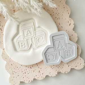 May include: A gray plastic cookie cutter shaped like three stacked blocks with the letters A, B, and C on each block.