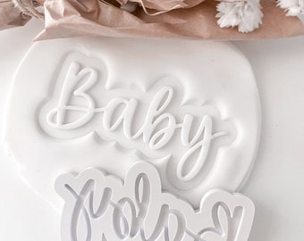 May include: White plastic cookie cutters with the words "Baby" and "yola" in a cursive font.