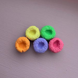 May include: Five small, round, colorful, textured, ceramic pots with a hole in the center. The pots are arranged in a semi-circle, with the yellow pot at the top, followed by green, purple, pink, and orange.