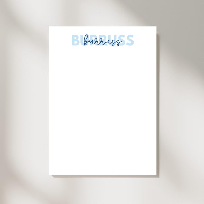 May include: A white notepad with the word "burruss" in blue script and block letters. The word "burruss" is centered at the top of the page. The notepad is rectangular and has a shadow on the right side.