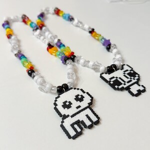 May include: Two beaded necklaces with rainbow colored beads and white beads. Each necklace has a pixelated white ghost charm with black eyes.