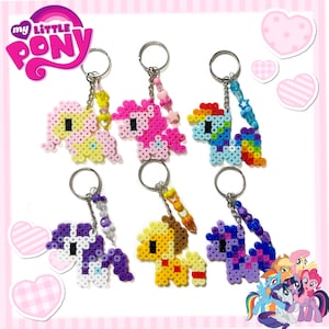 May include: Six My Little Pony keychains. Each keychain features a pony design made from colorful beads. The keychains have silver rings and beaded accents. The ponies are in various colors, including pink, yellow, blue, and purple.