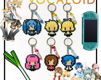 May include: A set of eight colorful beaded keychains featuring Vocaloid characters. Each keychain has a different character with their name spelled out in beads. The keychains are displayed on a white background with a green leek and a blue and green handheld gaming device.