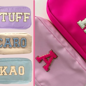 May include: Three zippered pouches with different colored fabric and personalized lettering. The pouches are lavender, beige, and light blue. The lettering is in gold and white.