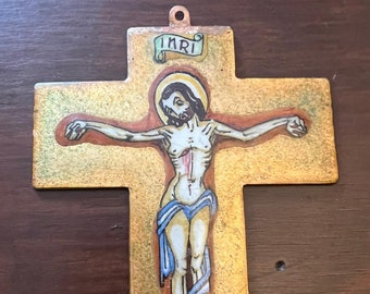 Może przedstawiać: Malowany metalowy krucyfiks ze złotym tłem. Postać Jezusa przedstawiona jest z aureolą, a krzyż u góry nosi napis "INRI". Dzieło sztuki zawiera czerwone, niebieskie i białe akcenty.