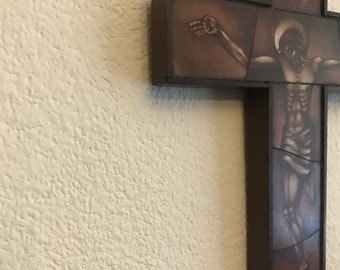 May include: A wooden cross with a painted image of Jesus Christ on the cross. The cross is brown with a dark brown border. The image depicts Jesus with a halo and the letters INRI at the top.
