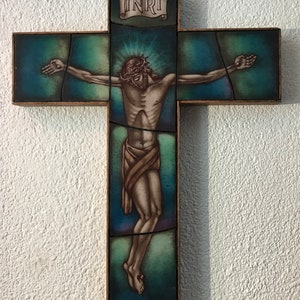 Może przedstawiać: Drewniany krzyż z witrażowym przedstawieniem Jezusa Chrystusa na krzyżu. Szkło jest mozaiką w kolorach niebieskim, zielonym i brązowym. Na szczycie krzyża widoczny jest napis "INRI".